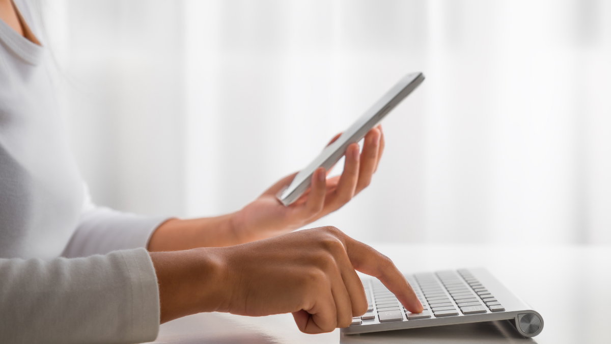 woman holding a phone in her hand and typing on keyboard